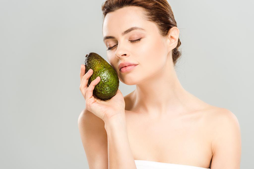  aantrekkelijke vrouw met gesloten ogen houden rijpe avocado geïsoleerd op grijs  - Foto, afbeelding