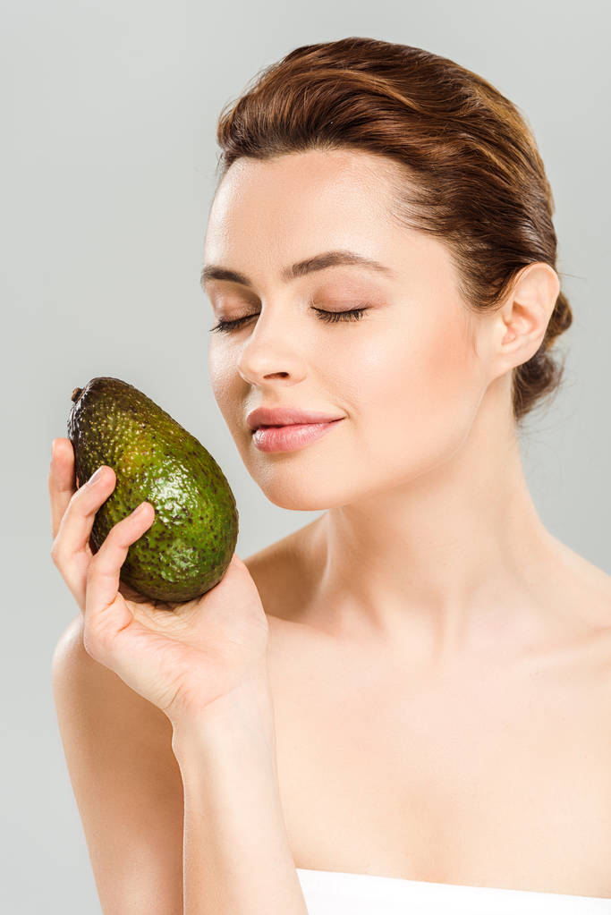 Gelukkige vrouw met gesloten ogen houden rijpe avocado geïsoleerd op grijs  - Foto, afbeelding