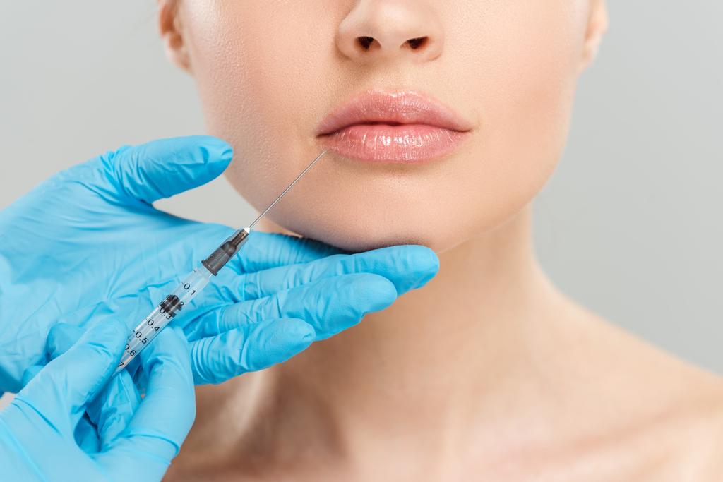visão recortada de cosmetologista segurando seringa perto da face da mulher isolada em cinza
  - Foto, Imagem