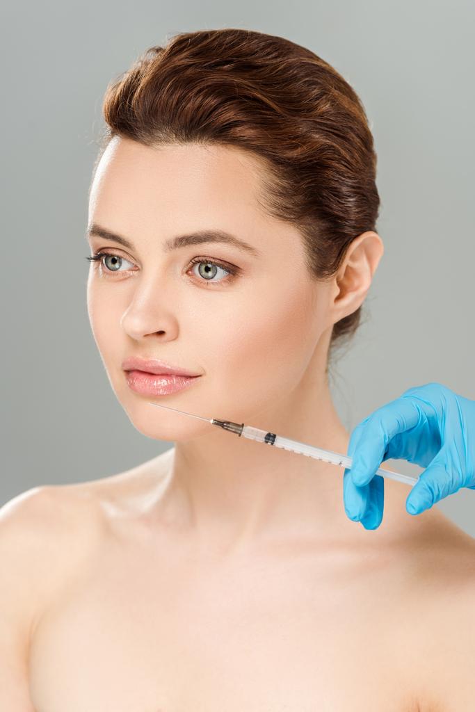 обрізаний вид косметолога тримає шприц біля обличчя оголеної і привабливої жінки ізольовані на сірому
  - Фото, зображення