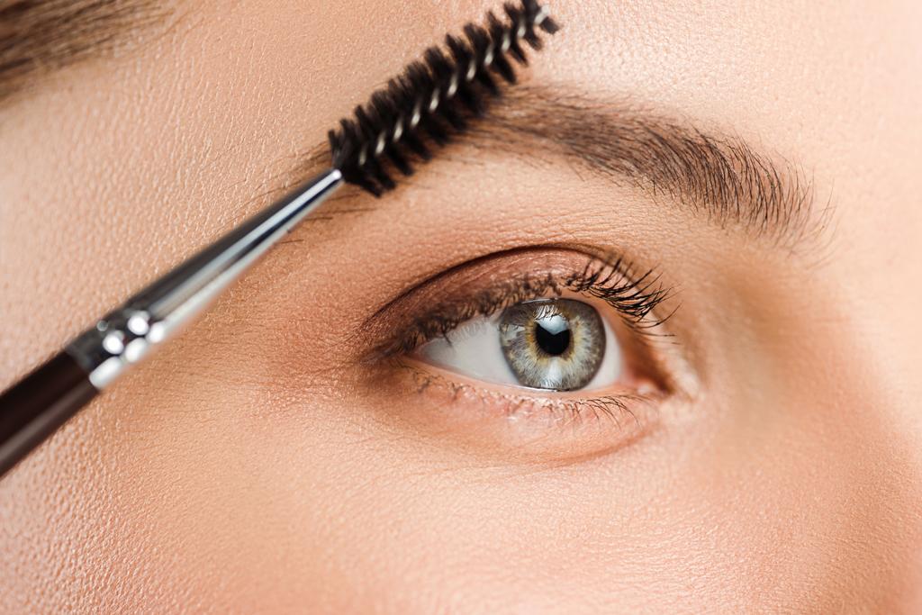 abgeschnittene Ansicht einer Frau mit Augenbrauenbürste in der Nähe der Augenbraue  - Foto, Bild