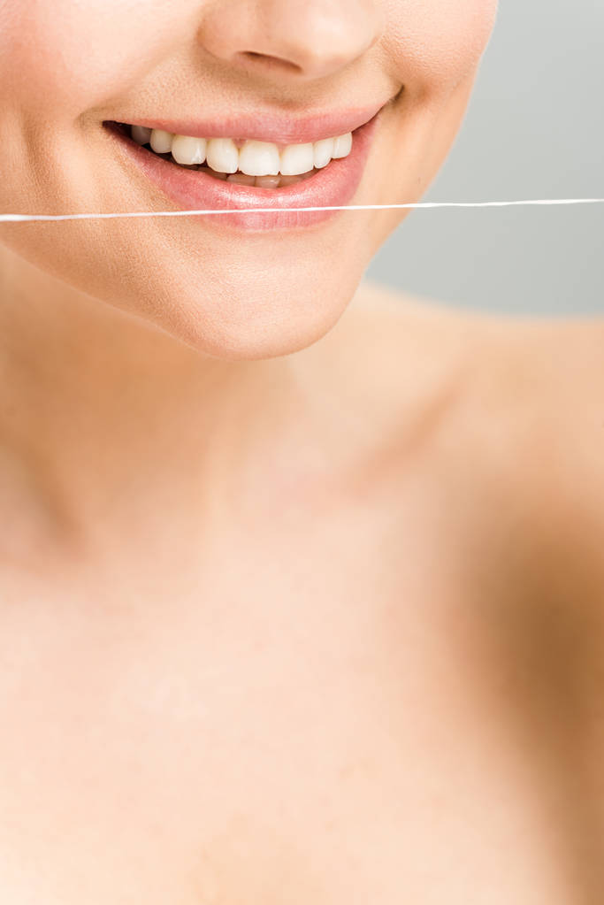 обрезанный вид счастливой голой женщины, держащей зубную нить рядом с зубами, изолированными на сером
  - Фото, изображение