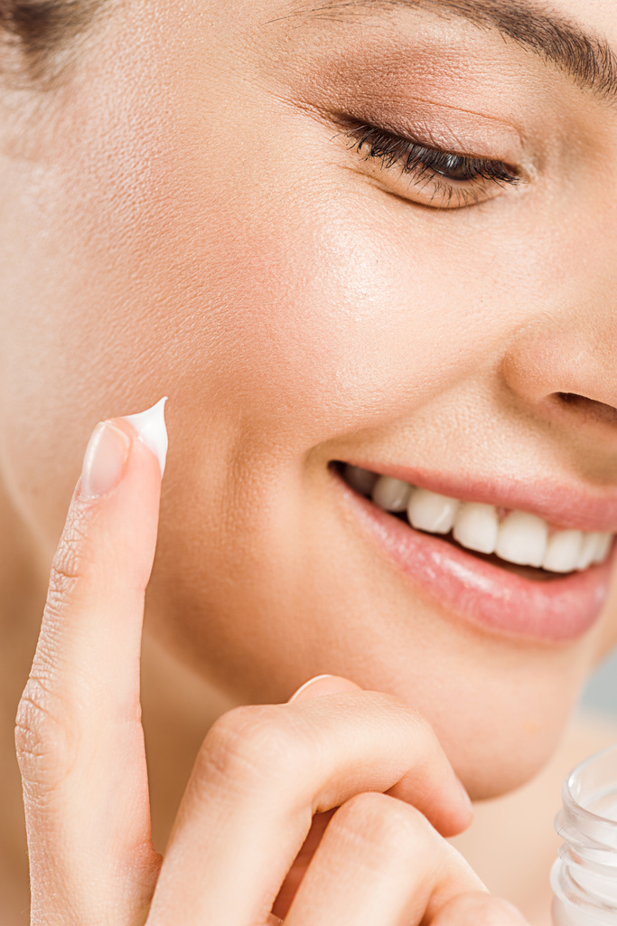 крупным планом веселая женщина улыбается во время нанесения крема для лица
  - Фото, изображение
