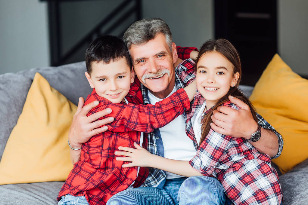 Feliz abuelo alegre sonriendo y sentado en el sofá con nietos
  - Foto, imagen
