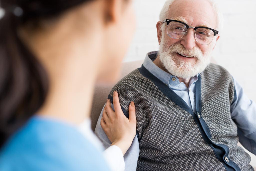 Selective focus of happy grey haired man looking at nurse - Photo, Image