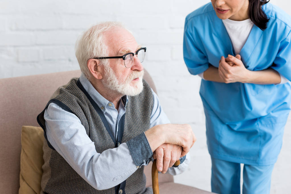 Vista cortada da enfermeira falando com o homem de cabelos grisalhos com bengala
  - Foto, Imagem