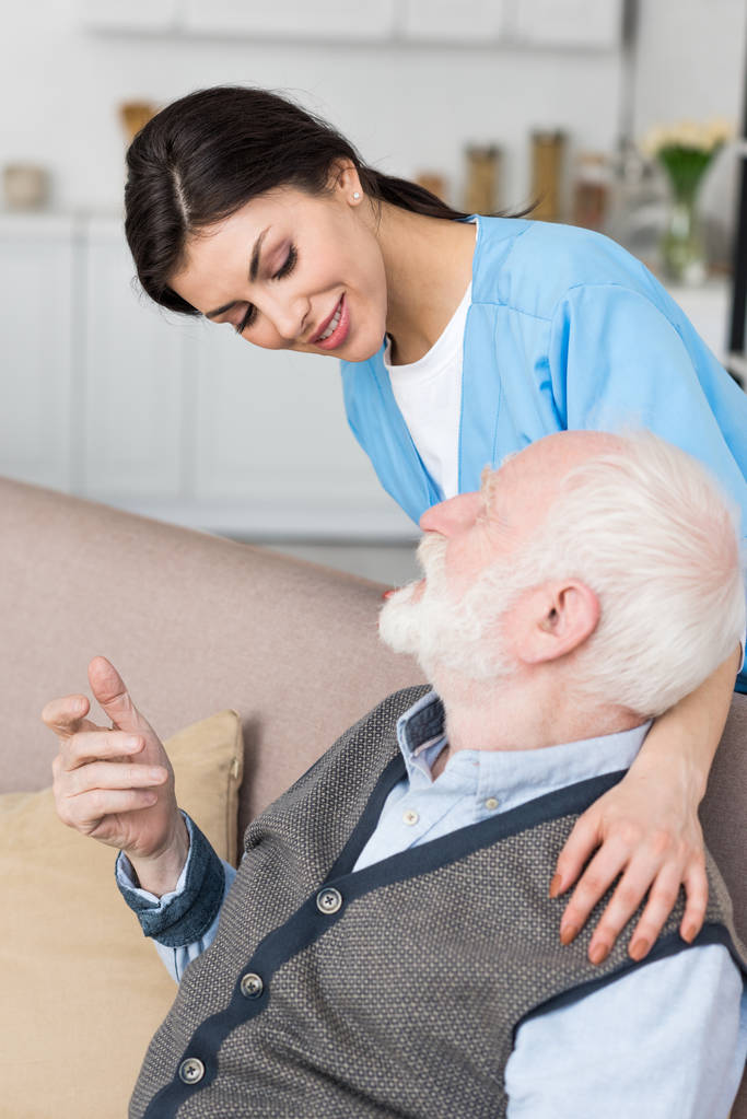 Smiling nurse putting hands on grey haired man - Photo, Image