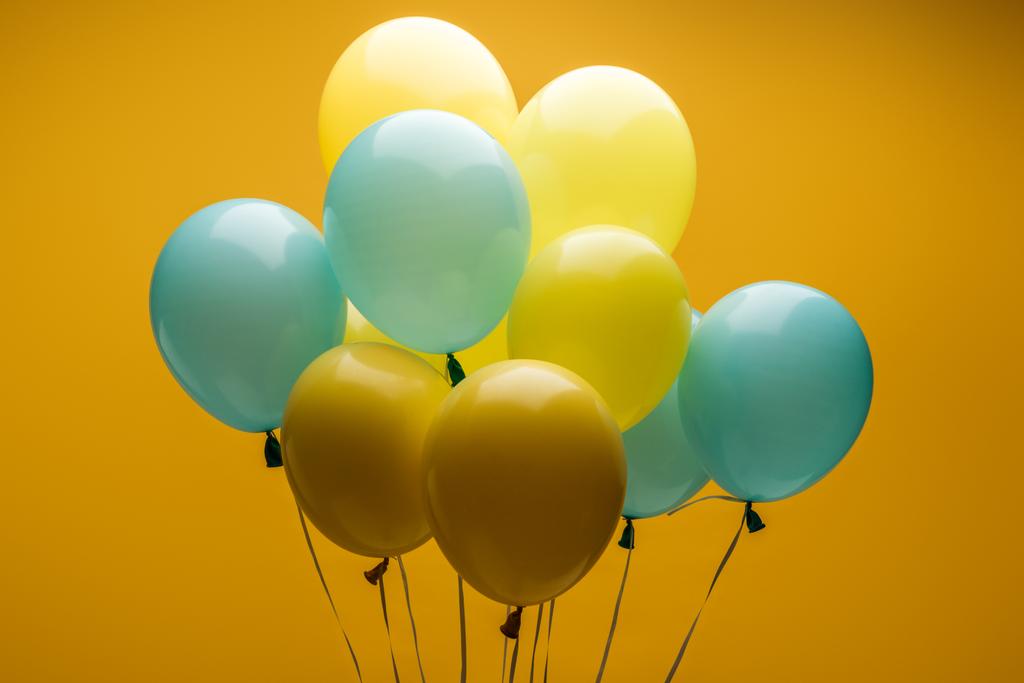 helle dekorative blaue und gelbe Luftballons auf gelbem Hintergrund - Foto, Bild