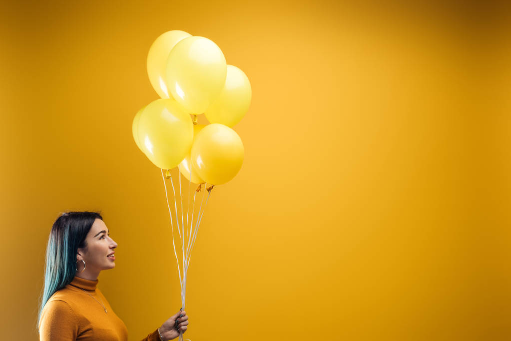 Lachende vrouw met feestelijke heldere decoratieve ballonnen op gele achtergrond - Foto, afbeelding