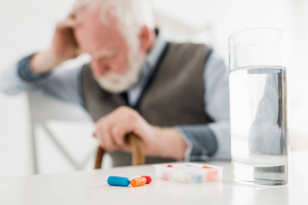 Foco seletivo de pílulas e água em vidro no fundo triste homem sênior
 - Foto, Imagem