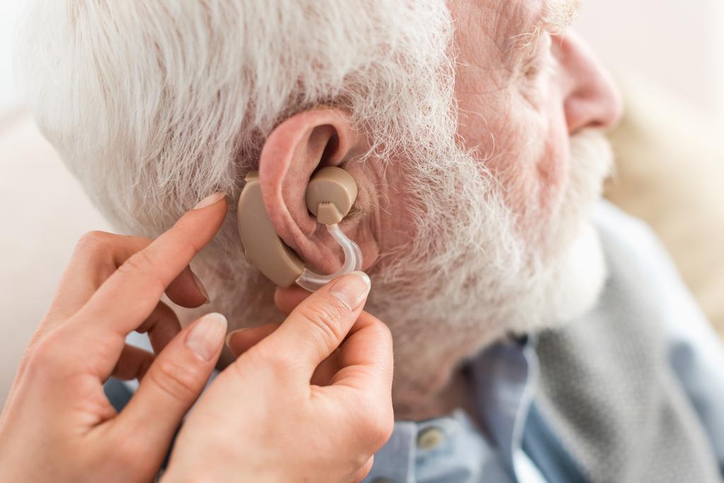 Обрізаний вигляд жінки, що допомагає сірому волосистому чоловікові, в слуховому апараті
 - Фото, зображення