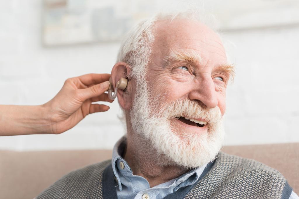 Hombre de pelo gris feliz con audífono, y mirando hacia otro lado
 - Foto, imagen