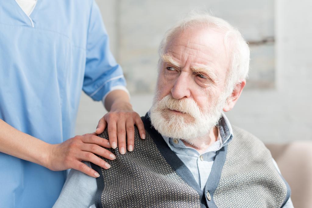 Медсестра кладе руки на плече сумного сіроволосатого чоловіка
 - Фото, зображення