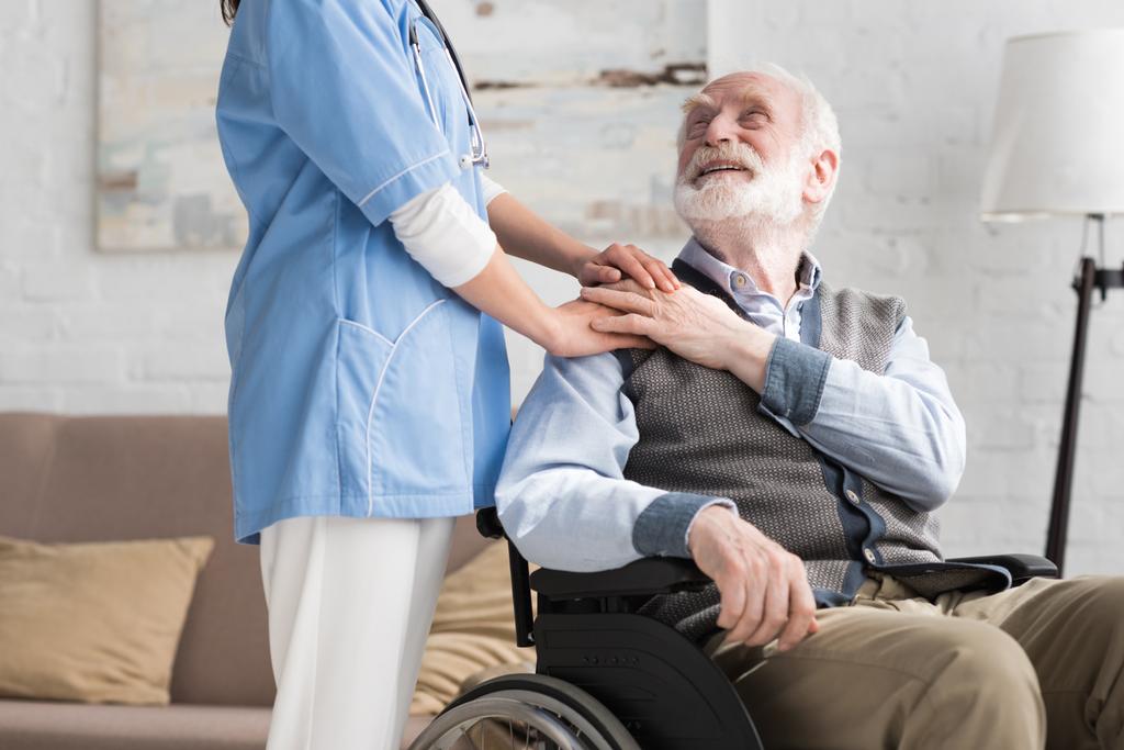 Hombre mayor feliz y discapacitado en silla de ruedas cogido de la mano con médico
 - Foto, Imagen