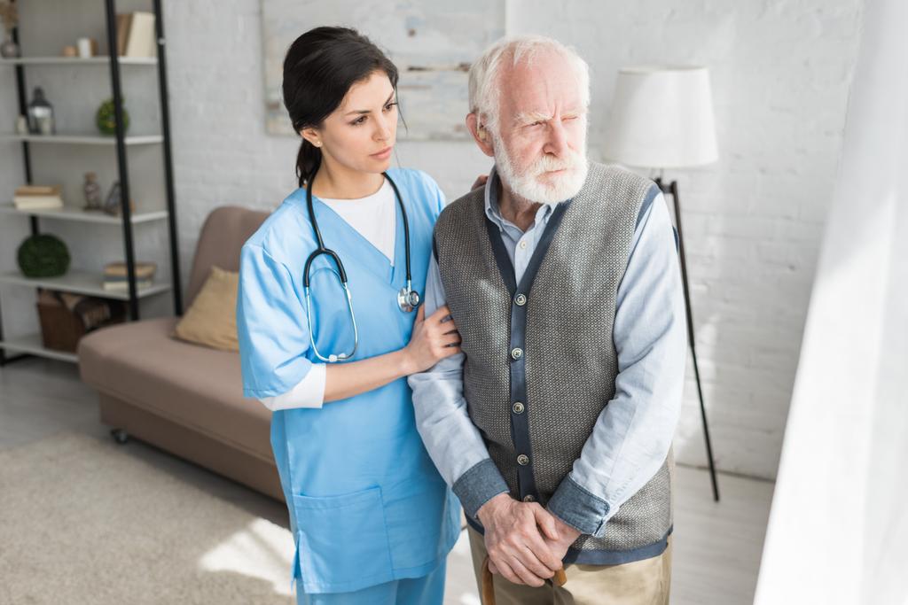 Medico di sostegno di uomo anziano, in piedi in una stanza luminosa, guardando da parte
 - Foto, immagini