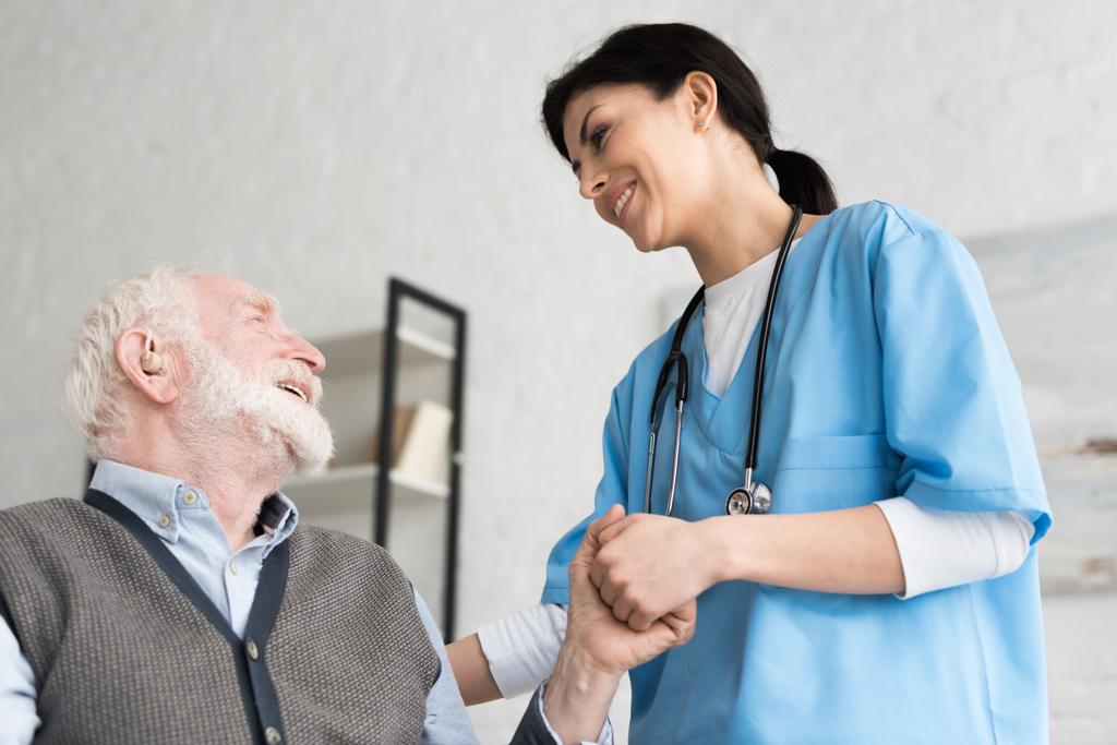 Vue à angle bas du médecin souriant, tenant la main avec un homme âgé
  - Photo, image