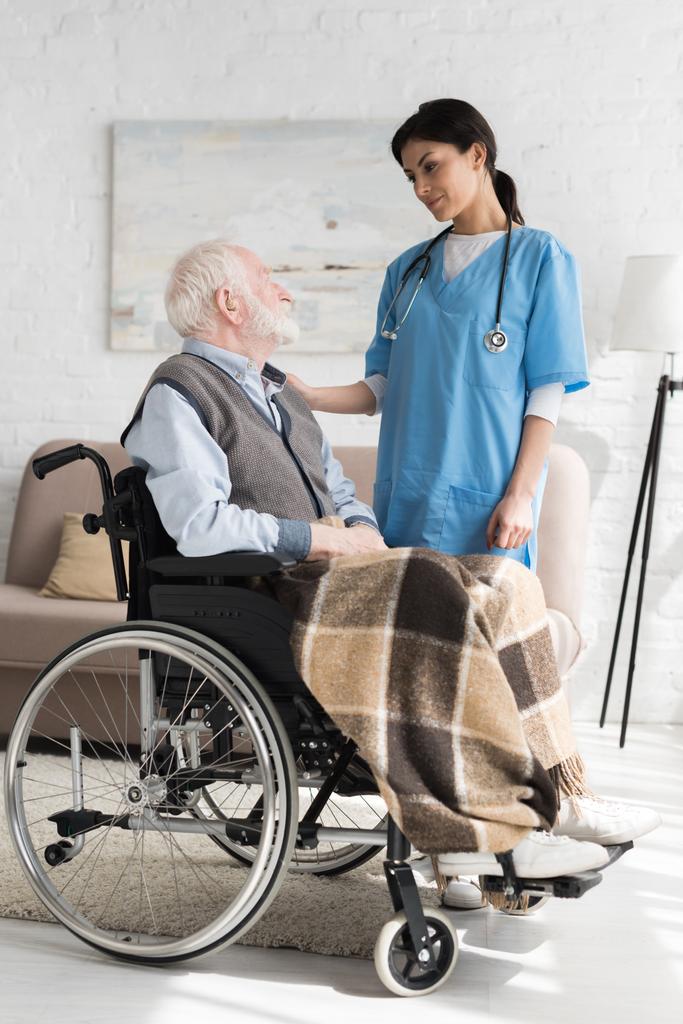 Медсестра накладає руки на інваліда сірого волохатого чоловіка в інвалідному візку
 - Фото, зображення