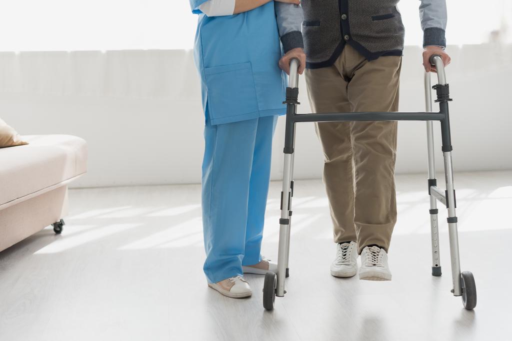 Обрезанный вид медсестры, идущей со старшим мужчиной в светлой комнате
 - Фото, изображение