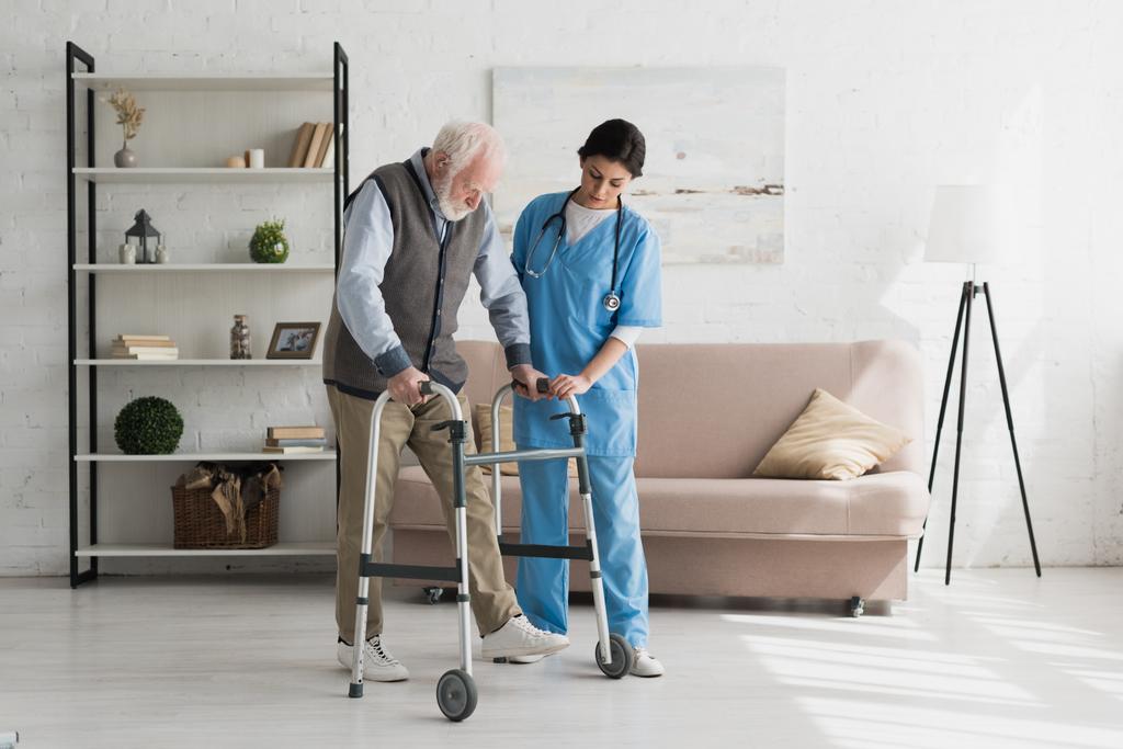 Verpleegkundige helpen om Senior man lopen thuis, herstellende na verwonding - Foto, afbeelding