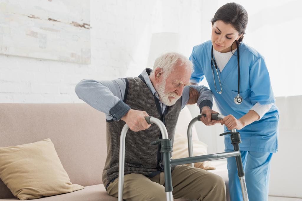 Arzt hilft Rentner beim Aufstehen vom Sofa - Foto, Bild