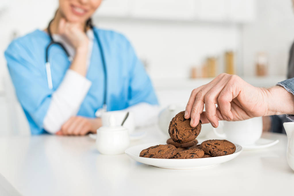 Selectieve focus van man hand met cookie en verpleegkundige op de achtergrond - Foto, afbeelding