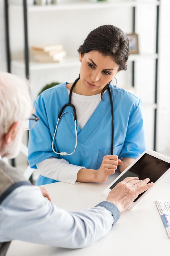 abgeschnittene Ansicht eines Rentners, der in der Nähe eines Arztes sitzt und ein digitales Tablet benutzt - Foto, Bild