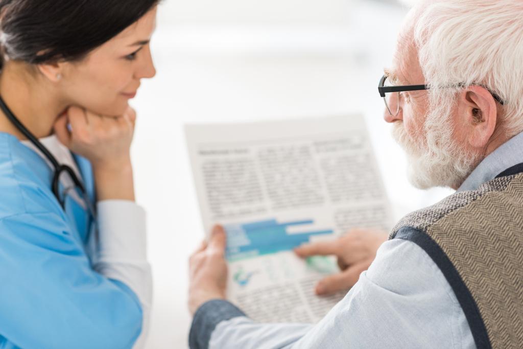 Selective focus of grey haired man talking with nurse, holding newspaper in hands - Photo, Image