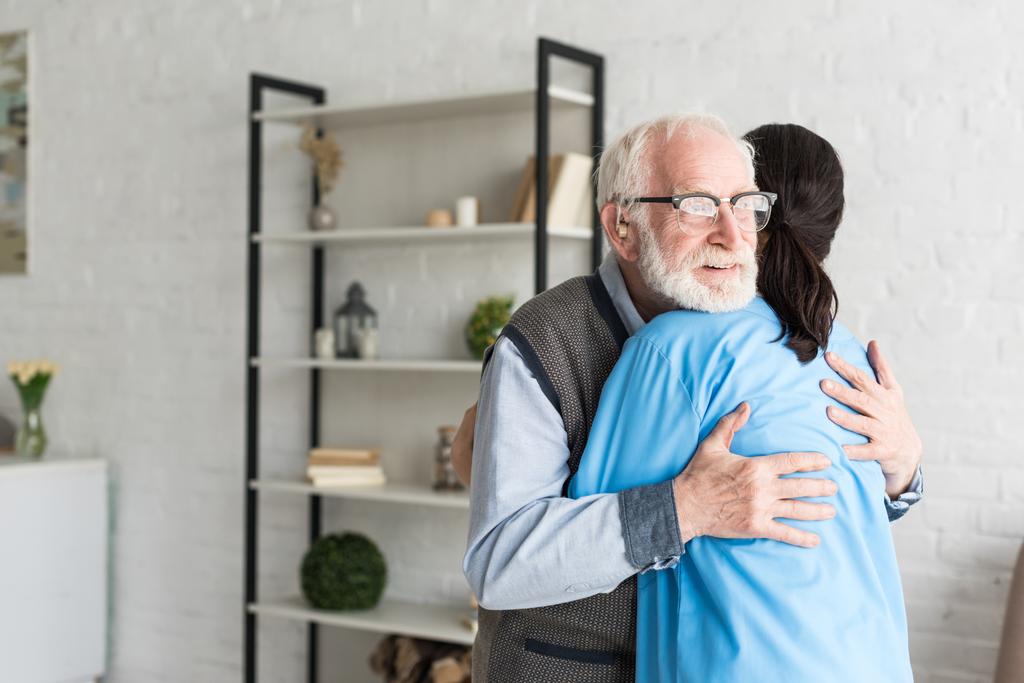 Gelukkige gepensioneerde man knuffelen met arts, staande in fel lichtkamer - Foto, afbeelding