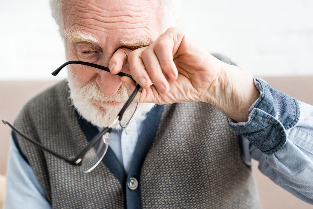 Грустный пожилой человек, держащий очки, и закрывающий глаза на руке
 - Фото, изображение