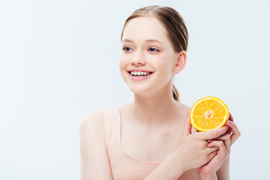 boldog mosolygó tinédzser gazdaság narancssárga felét, és elnézett elszigetelt szürke - Fotó, kép