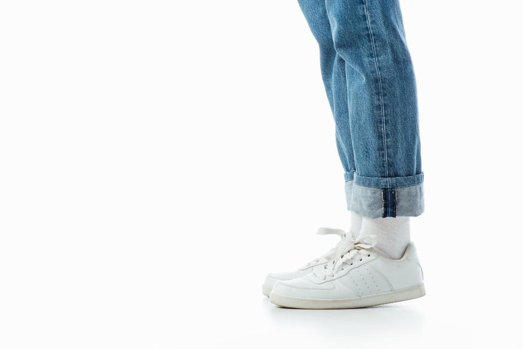 Ausgeschnittene Ansicht von Teenagerbeinen in weißen Turnschuhen und blauen Jeans isoliert auf weißem Grund - Foto, Bild