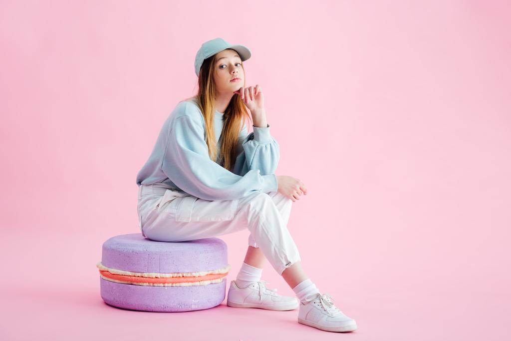 bella ragazza adolescente in berretto seduto su macaron decorativo su rosa
 - Foto, immagini