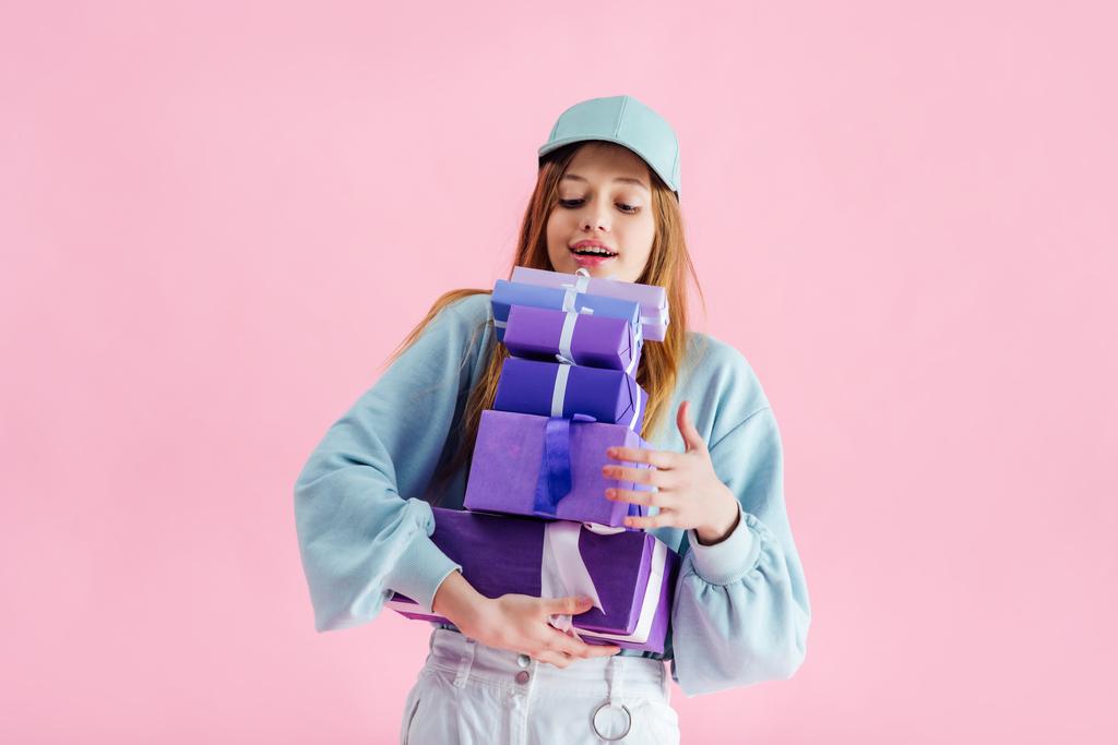 счастливая красивая девочка-подросток в кепке держит подарочные коробки изолированы на розовый
 - Фото, изображение