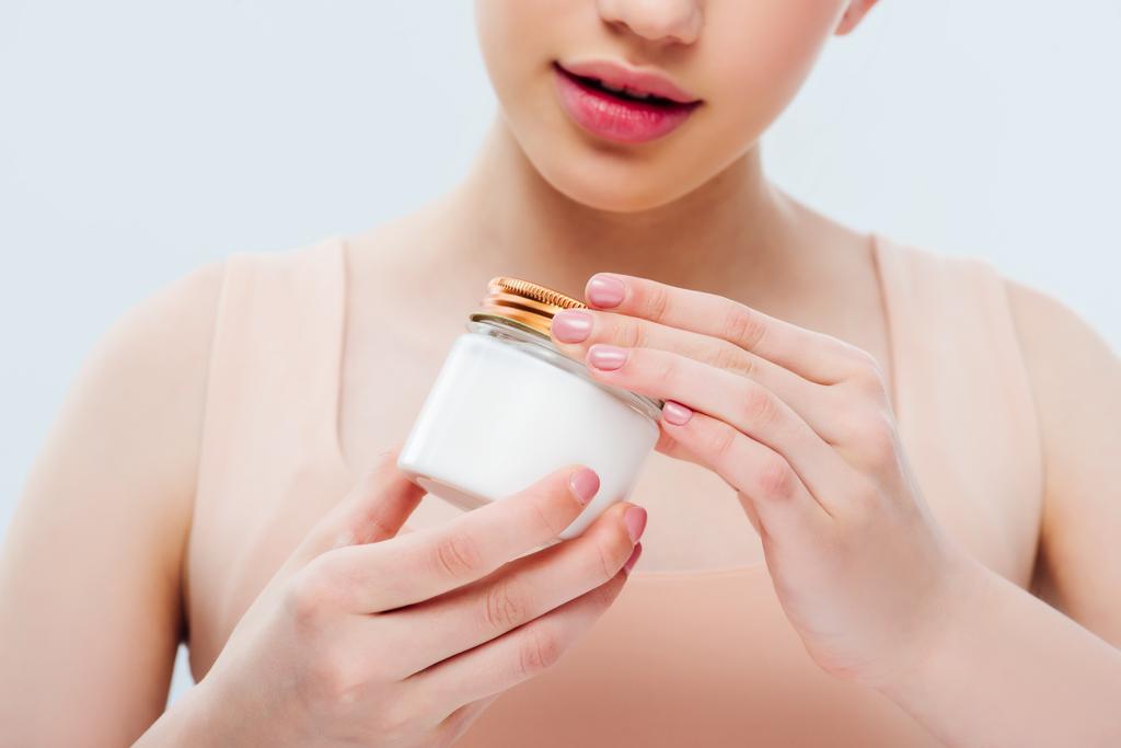 bijgesneden weergave van tiener meisje bedrijf cosmetische crème in handen geïsoleerd op grijs - Foto, afbeelding