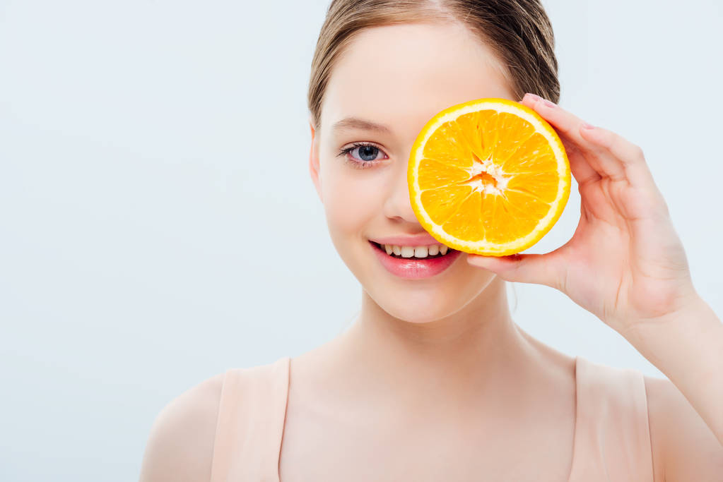 adolescente con sonrisa sosteniendo maduro naranja medio cerca de la cara aislado en gris
 - Foto, Imagen