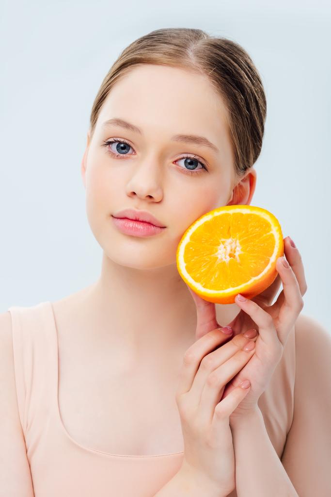 όμορφη έφηβη κορίτσι κρατώντας ώριμο πορτοκαλί μισό απομονώνεται σε γκρι - Φωτογραφία, εικόνα