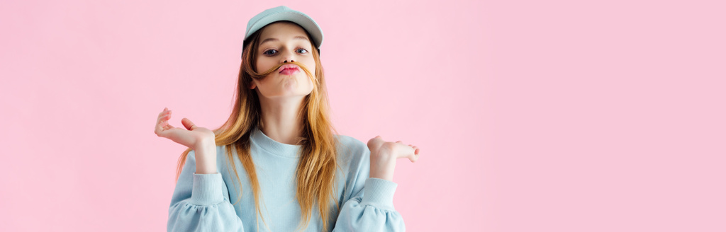 panoramic shot of pretty teenage girl in cap with mustache of hair grimacing isolated on pink - Photo, Image