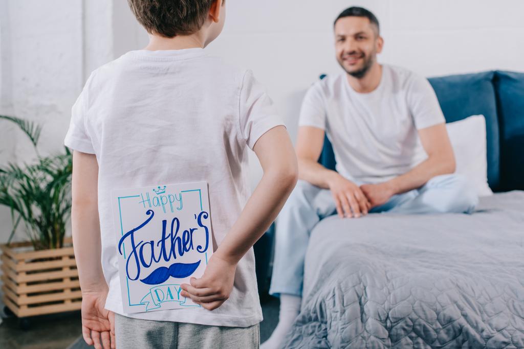 selektywne skupienie dziecka trzyma Ojcowie dzień karty okolicznościowe za plecami, stojąc przed szczęśliwym ojcem  - Zdjęcie, obraz