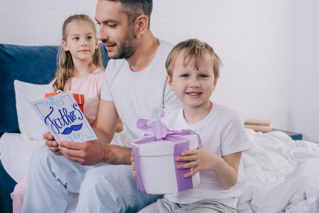 adorabile figlia e figlio seduto con scatole regalo vicino felice papà in possesso di padri giorno biglietto di auguri
 - Foto, immagini