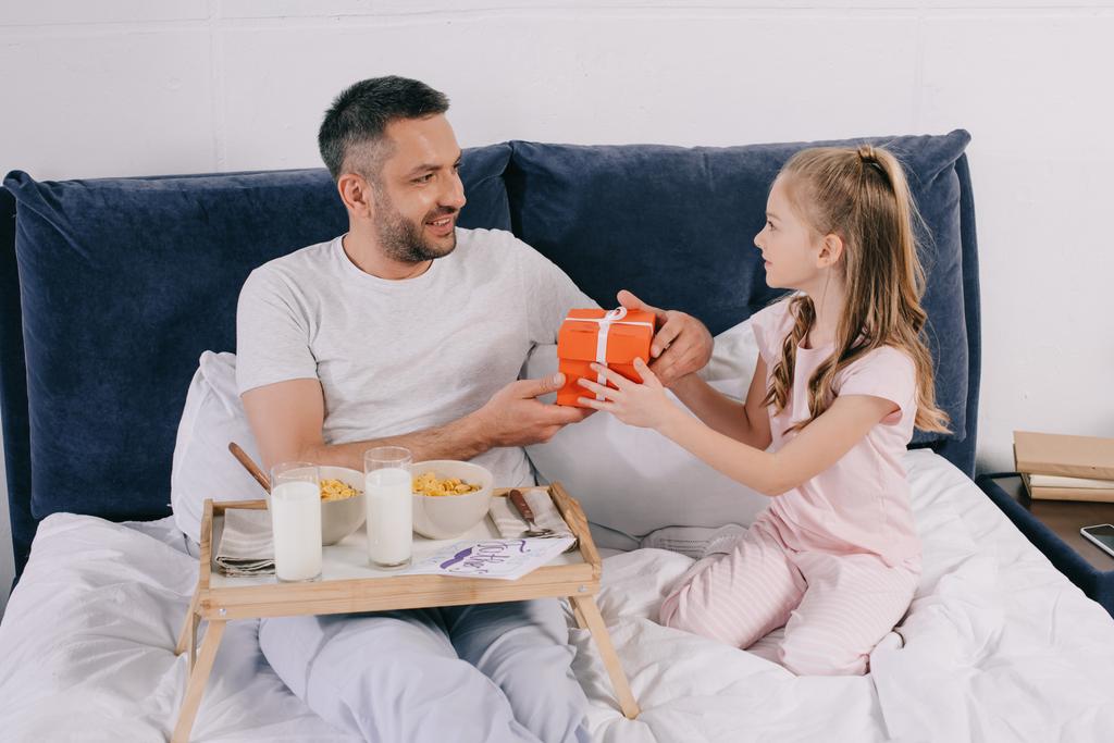 Niedliches Kind schenkt Papa einen Geschenkkarton zum Vatertag beim Frühstück im Bett - Foto, Bild
