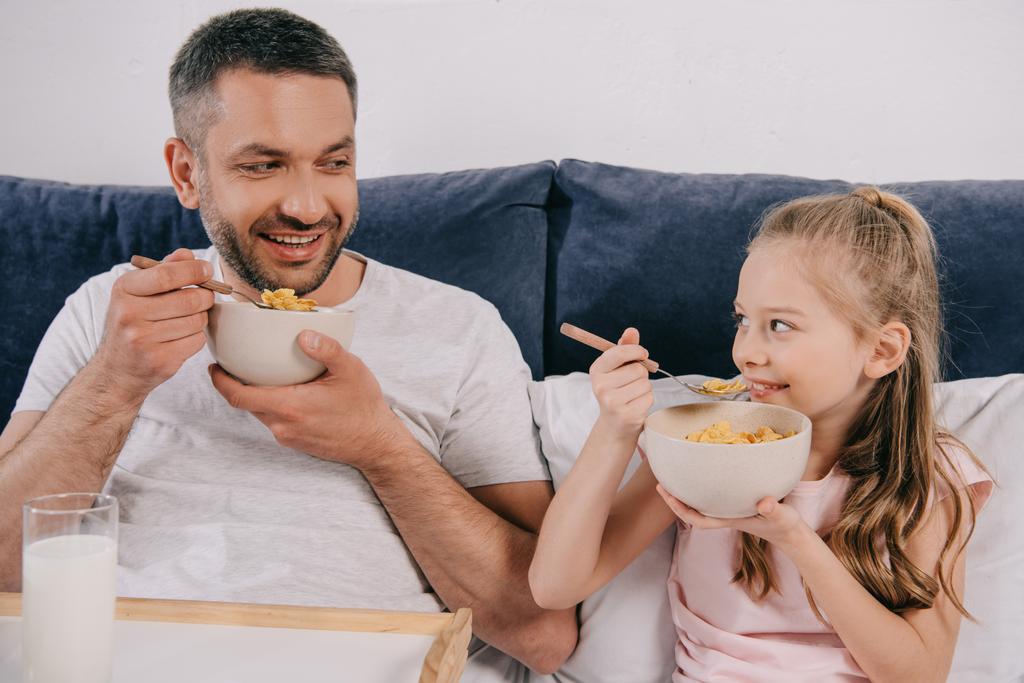 cheerful dad with adorable daughter having breakfast in bed on fathers day together - Foto, afbeelding