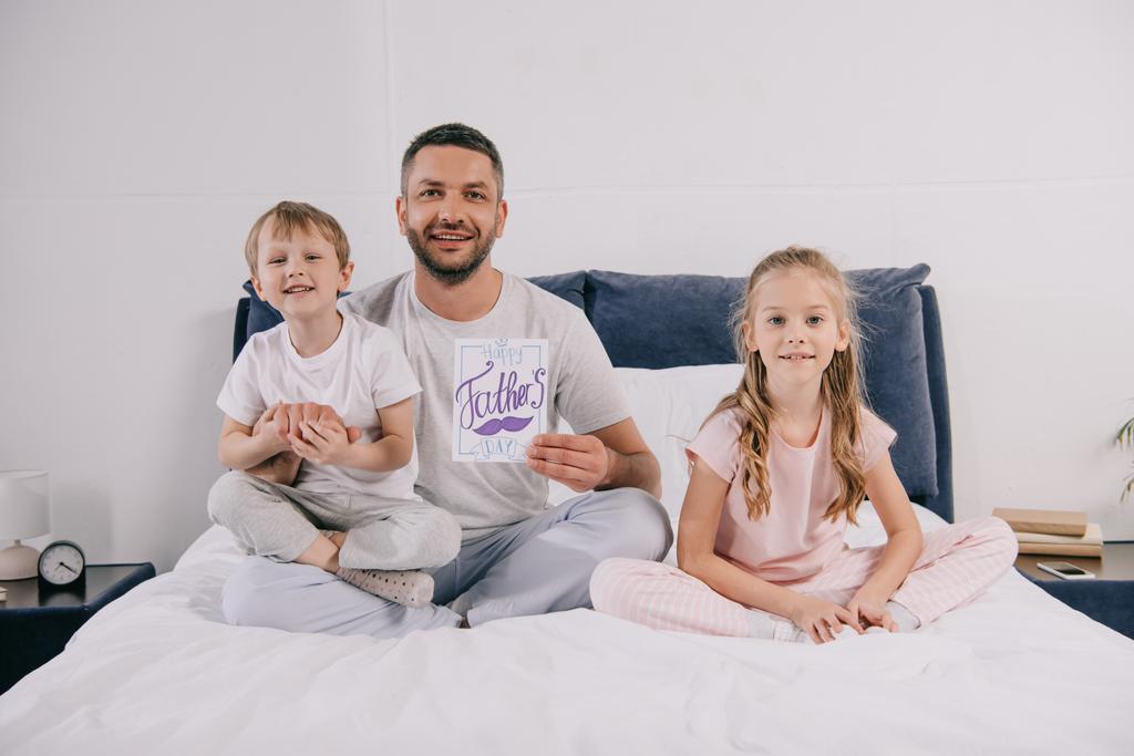 pai feliz segurando pai cartão de saudação dia enquanto sentado na cama perto de crianças adoráveis
 - Foto, Imagem