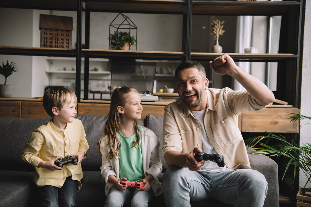 キエフ, ウクライナ - 5月 10, 2019: 幸せな家族は、勝者のジェスチャーを示しながら、ジョイスティックでビデオゲームをプレイ. - 写真・画像