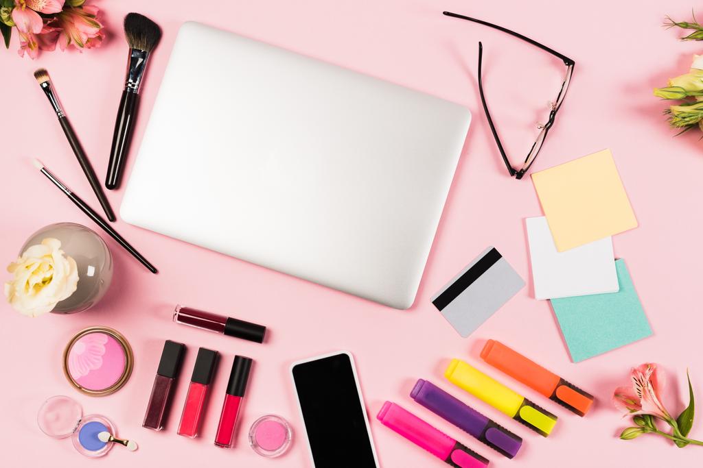 felső kilátás-ból laptop, Smartphone-val üres képernyő, hitelkártya, szemüveg, virágok és dekoratív kozmetikai-ra rózsaszín - Fotó, kép