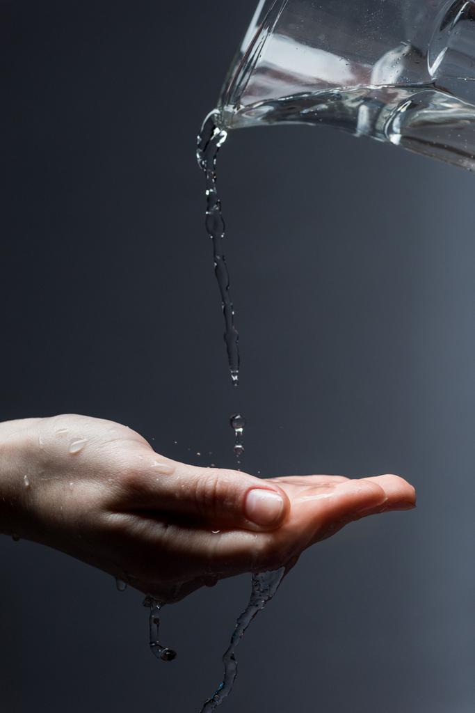 abgeschnittene Ansicht einer Frau mit Krug und fließendem Wasser auf dunklem Grund - Foto, Bild