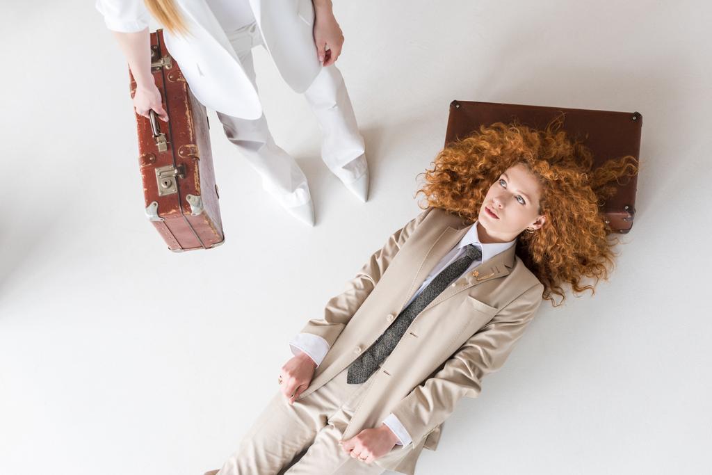Top view of redhead woman lying near girl standing with suitcase on white
  - Фото, изображение