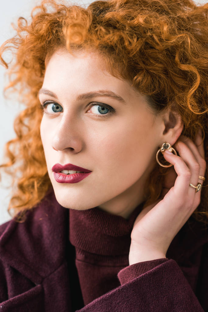 close up of attractive curly redhead woman looking at camera and touching hair - Photo, Image