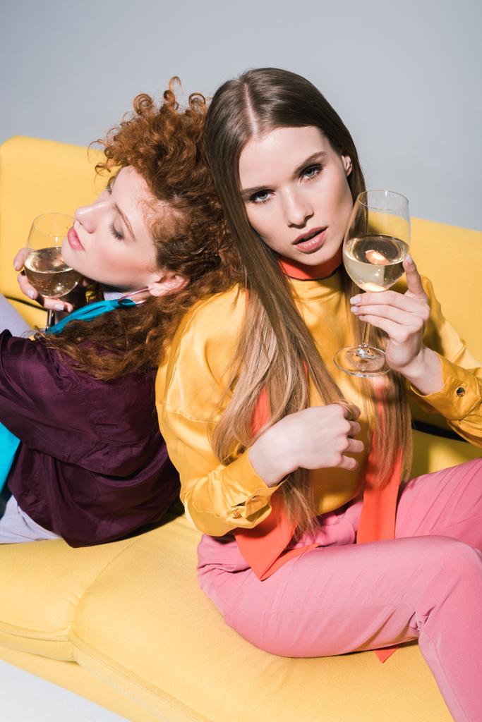 Overhead-Ansicht des rothaarigen Mädchens in der Nähe blonde Frau mit Champagnerglas sitzt auf gelbem Sofa auf weiß  - Foto, Bild