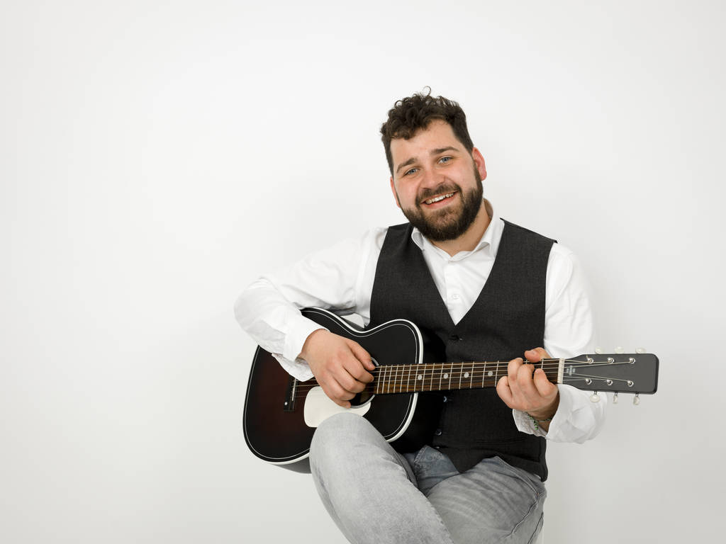 homem com cabelo preto e barba tocando guitarra acústica no fundo branco
 - Foto, Imagem