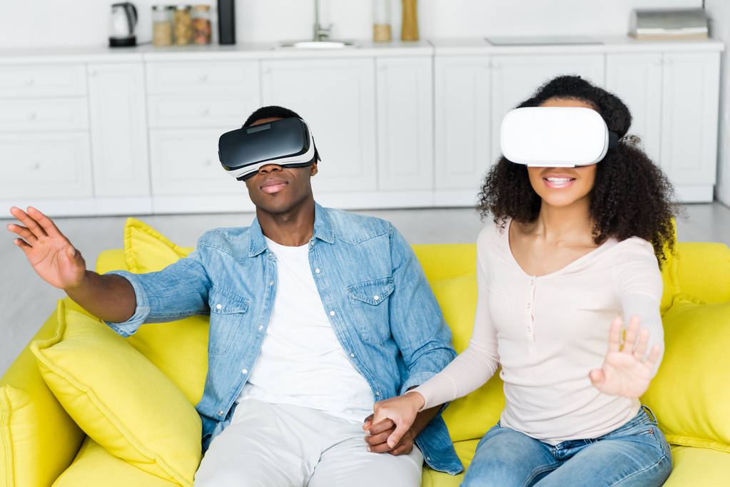 Αφρικάνικο ζευγάρι σε VR ακουστικά που κάθονται στον καναπέ - Φωτογραφία, εικόνα